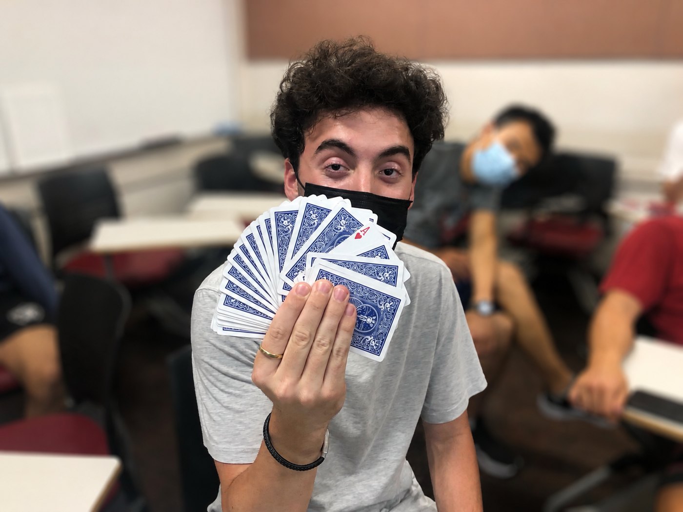 Tyler in a face mask fanning a deck of blue playing cards toward the camera, one ace flipped face-up.