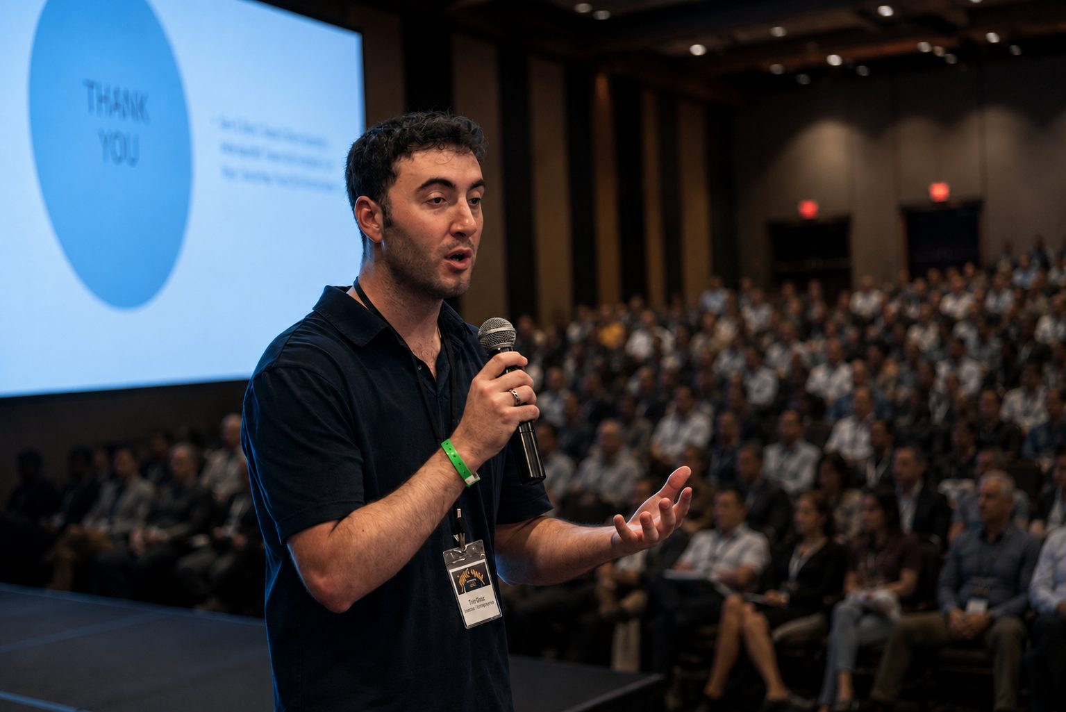 Tyler Gibgot on stage with a microphone, speaking to a large seated conference audience.