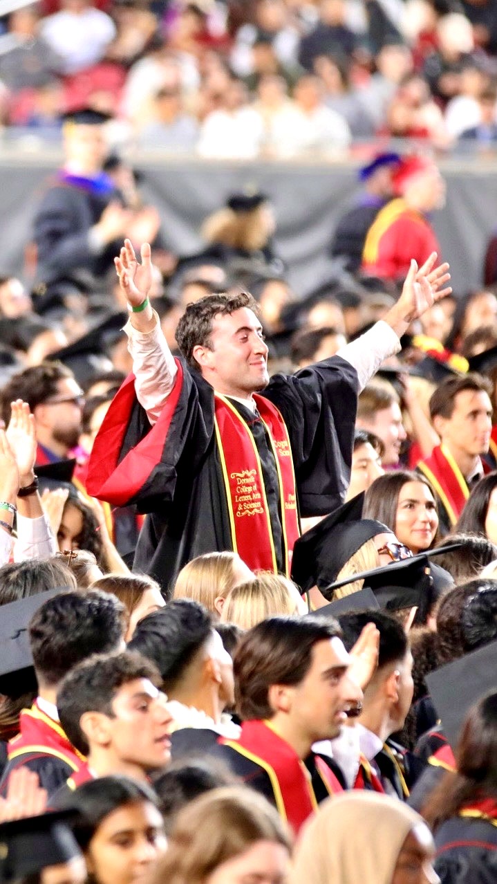Tyler standing with both arms raised in celebration among the crowd at USC's 2025 commencement.