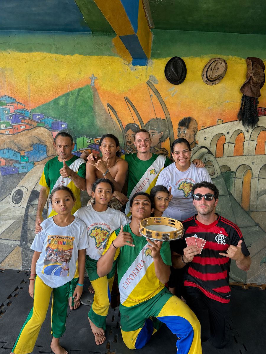 Tyler Gibgot holding playing cards with a capoeira group of kids and instructors in front of a painted mural in Brazil.