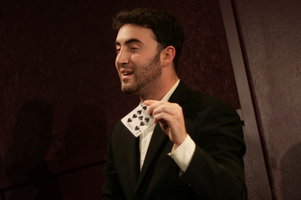 Tyler Gibgot on stage holding up a single playing card toward the audience.