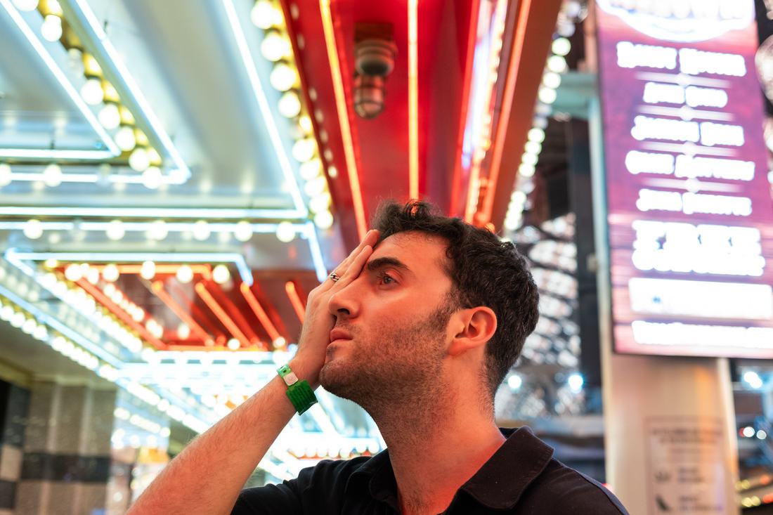 Tyler covering his left eye with his hand beneath neon casino lights.