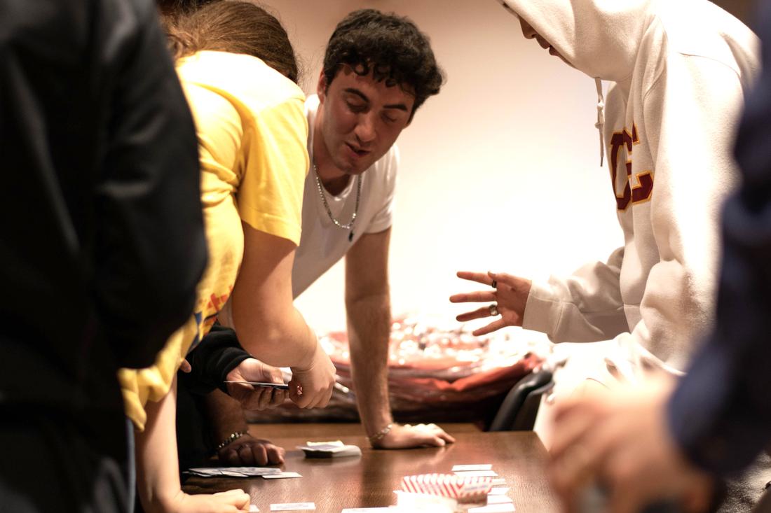 Tyler Gibgot performing card magic at a table surrounded by students.