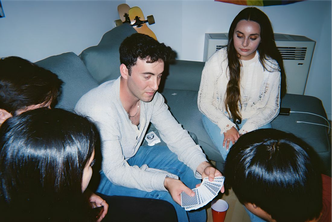 Tyler Gibgot seated on a couch fanning a deck of cards for a small group of friends leaning in around him.