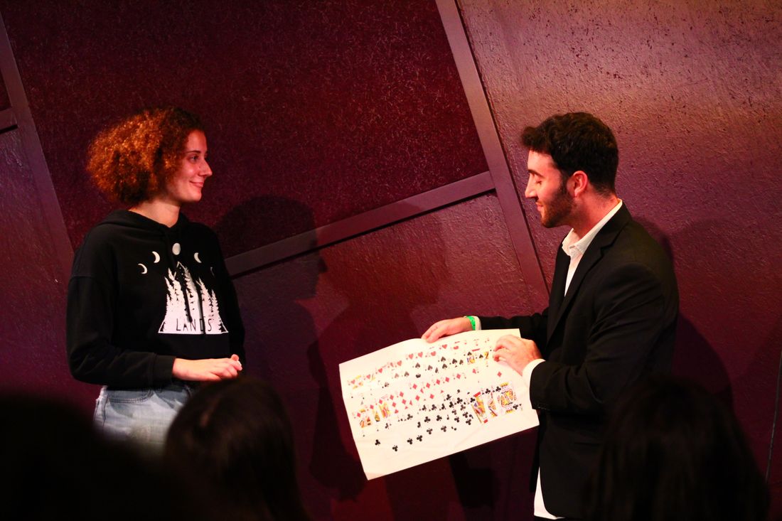 Tyler Gibgot on stage showing a volunteer a cloth printed with a full deck of cards.