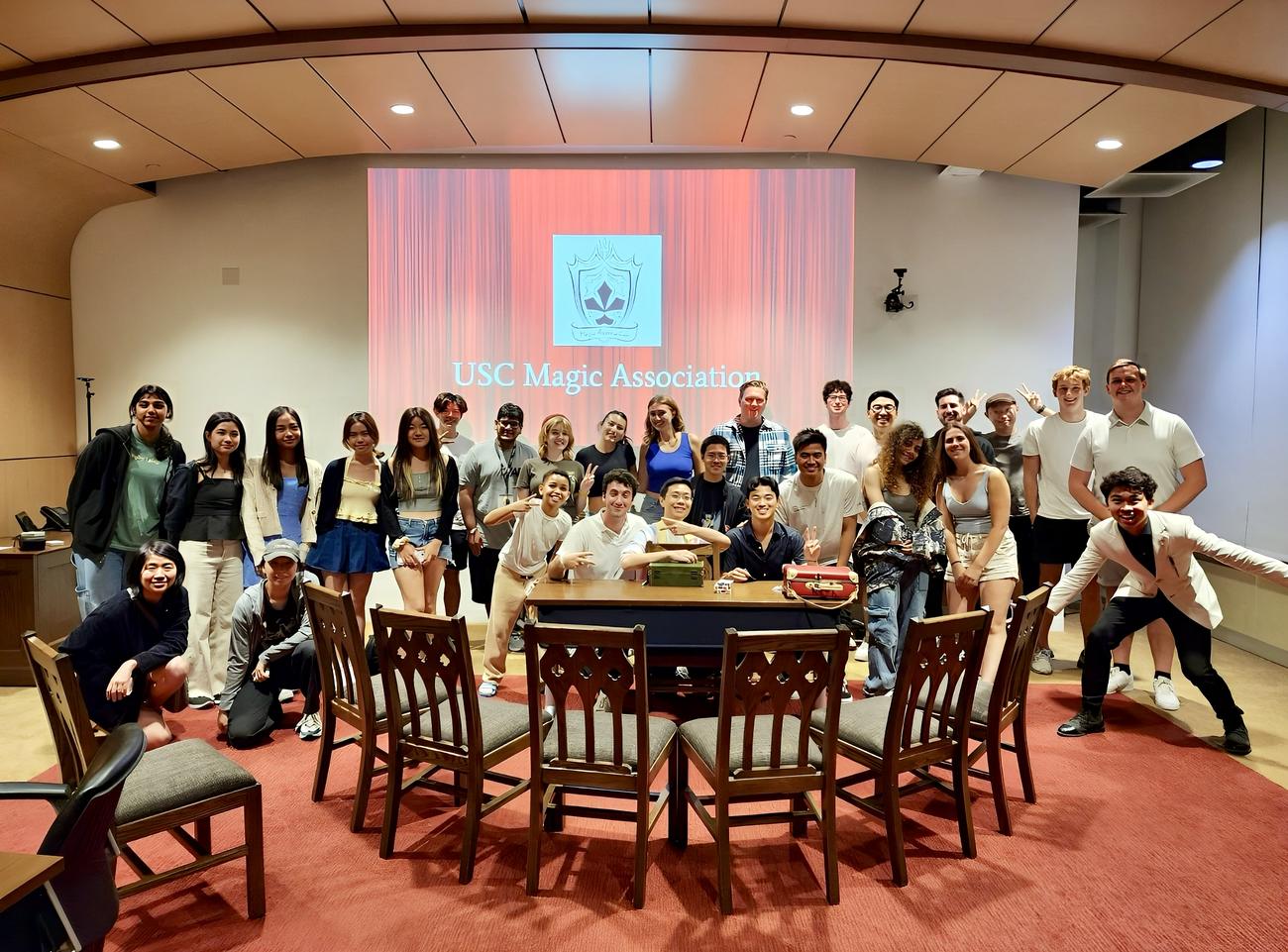 A large group photo of USC Magic Association members gathered around a performance table.